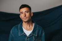 a man in a denim jacket standing in front of a blue cloth