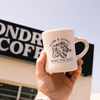 a person holding up a coffee mug that says win the race